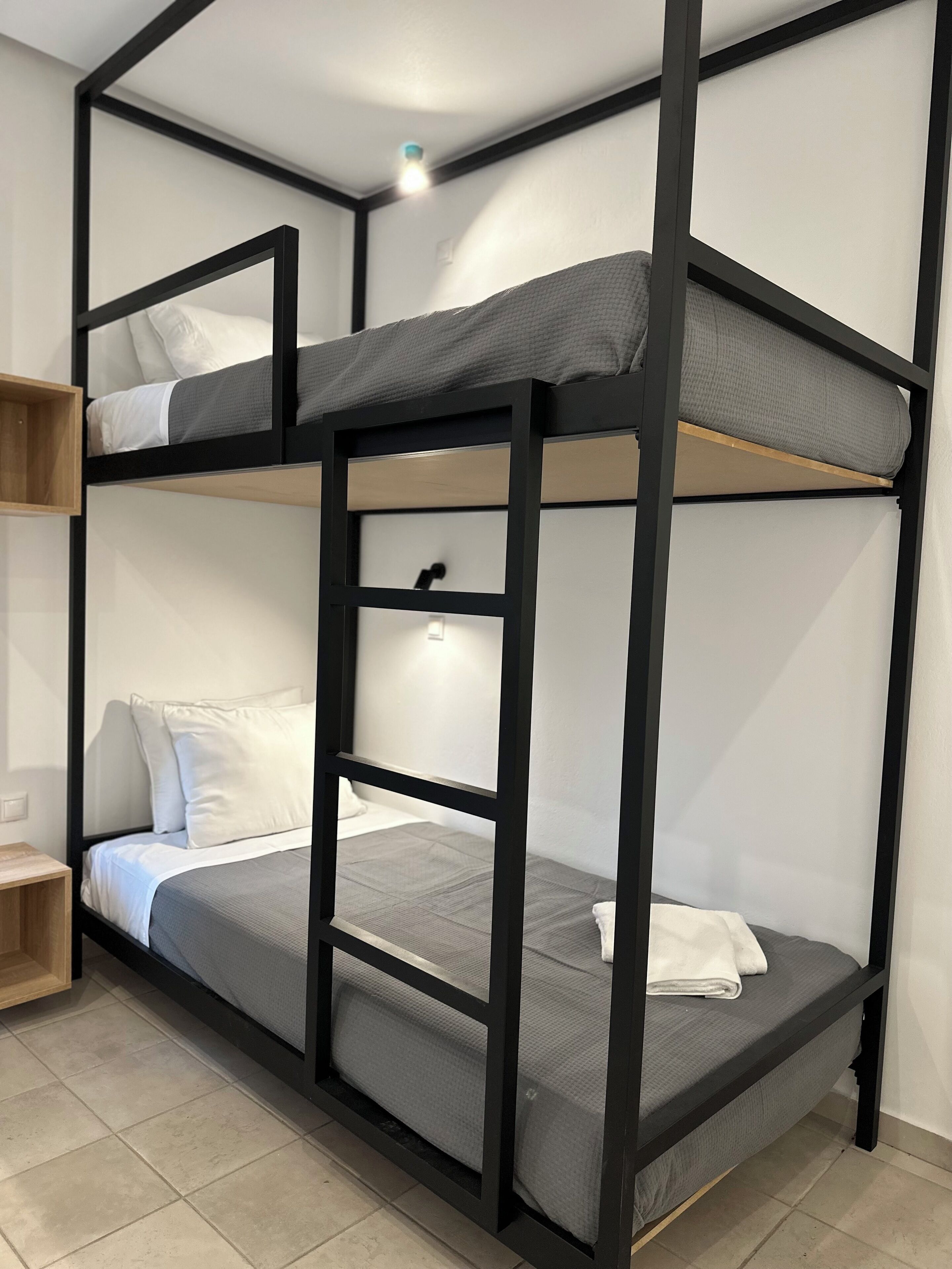 A bunk bed with two levels, a wooden shelf, and a small bedside table.