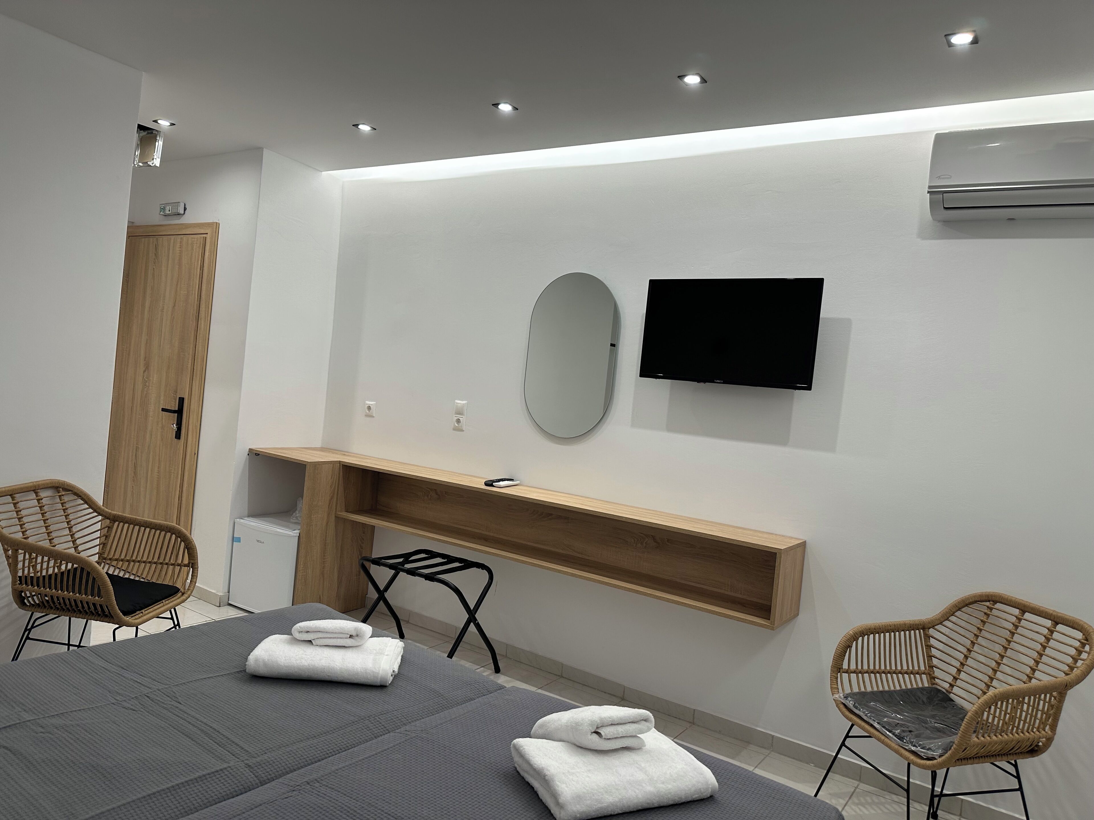 Una camera d'albergo moderna con un letto, due poltrone in vimini, una toeletta in legno, un televisore a schermo piatto e un condizionatore d'aria.