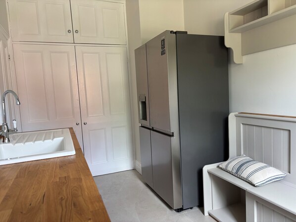 A kitchen with a stainless steel refrigerator, white cabinetry, a wooden countertop, and a built-in bench with a pillow.