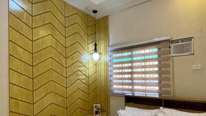 A hotel room with a bed, a nightstand, a wall with a geometric pattern, a hanging light, and a window with blinds. - Francheska Suite: Minimalist Comfort Near Cavinti’s Natural Wonders (Cavinti)
