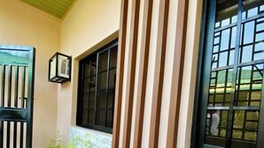 Fachada de un edificio con suelo de baldosas, una verja negra, una ventana con diseño de cuadrícula y una jardinera con plantas.