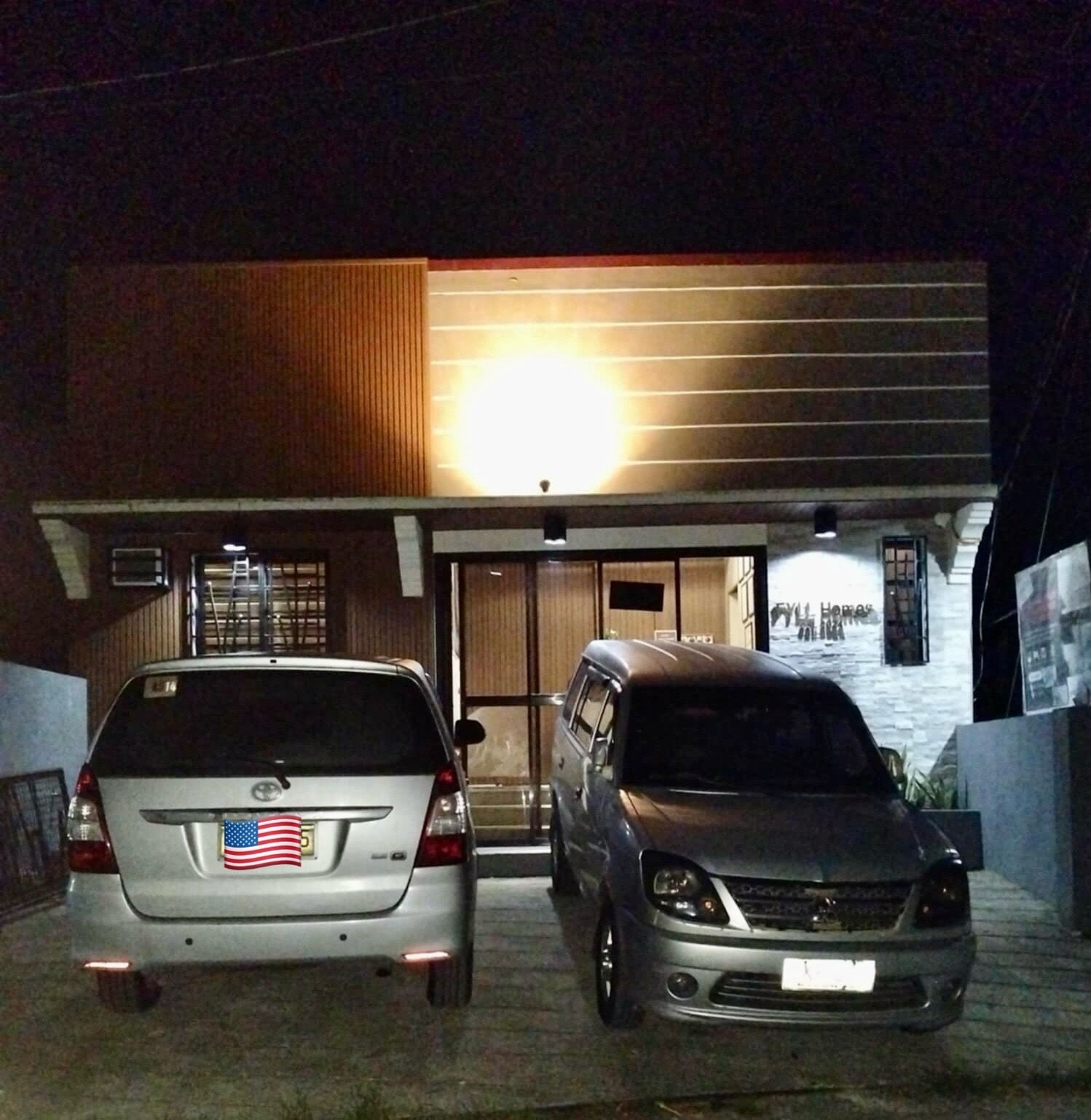 Two cars parked in front of a building with a large light above the entrance.