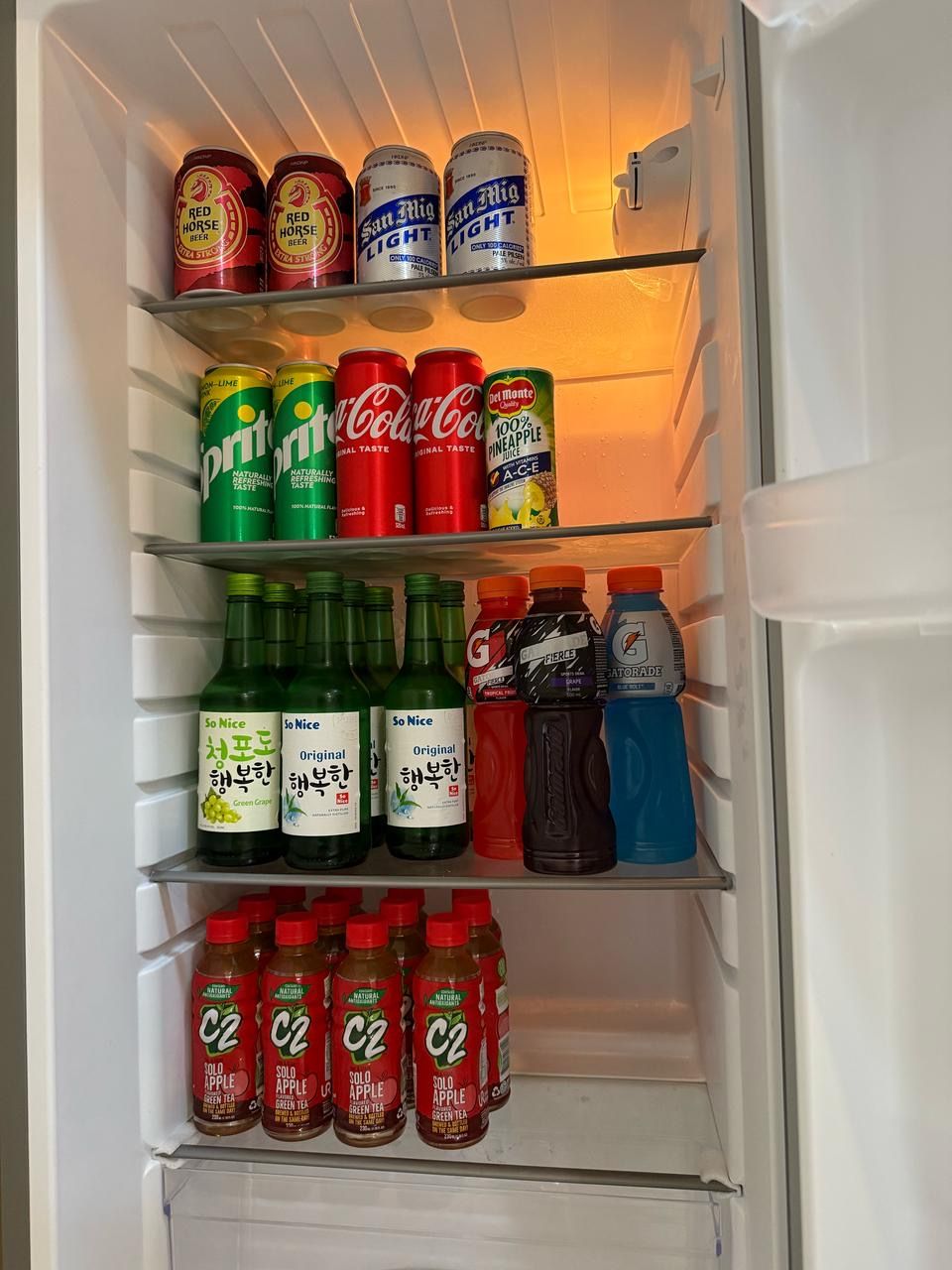 Et køleskab fyldt med forskellige drikkevarer, herunder Red Horse øl, San Mig Light øl, Sprite, Coca-Cola, Del Monte ananasjuice, So Nice grønne druesaft, So Nice original grønne druesaft, Gatorade og C2 grøn te.
