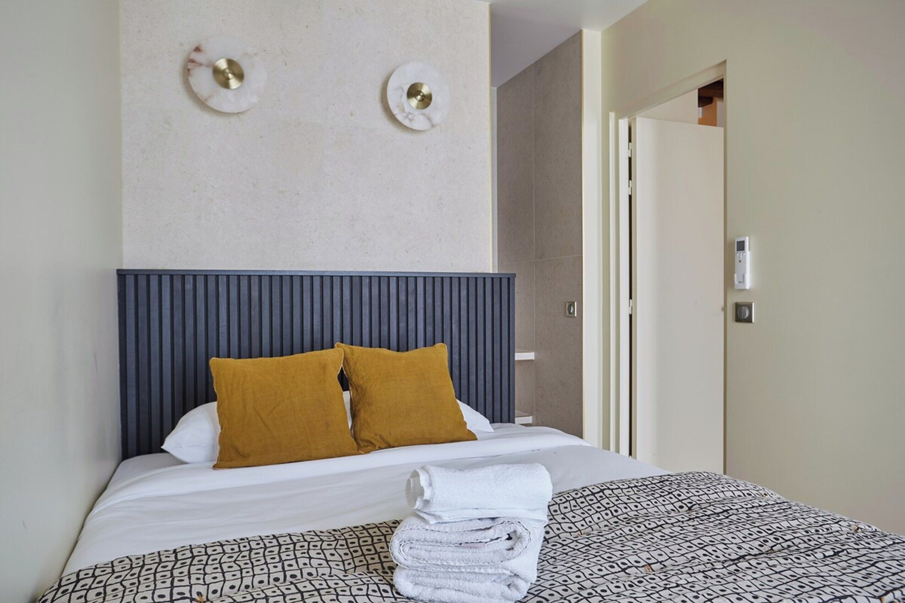 A neatly made bed with a patterned bedspread, two pillows, and a folded towel.