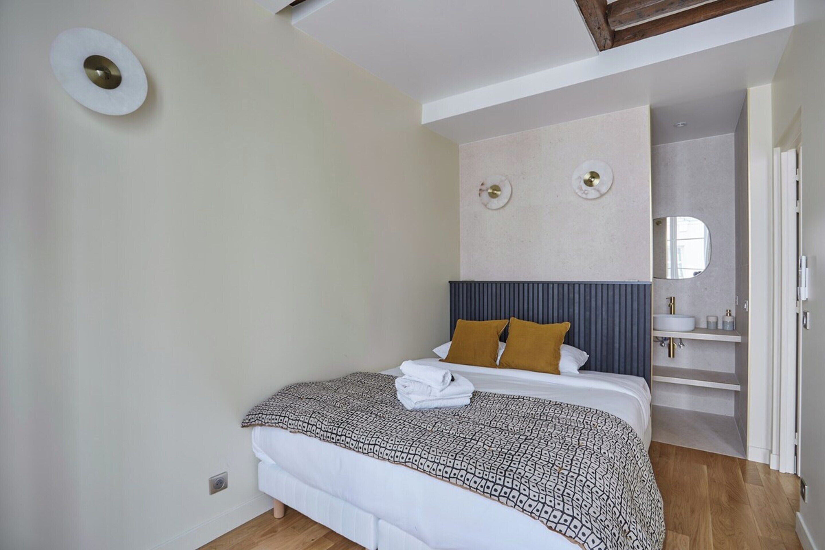 A modern bedroom with a bed, a headboard, a bedside table, and a built-in shelf with toiletries.