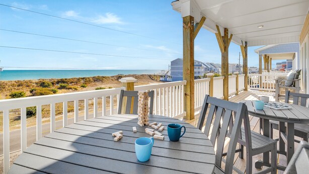 Eine Holzterrasse mit Blick auf den Strand, Sitzgelegenheiten im Freien und einem weißen Geländer.