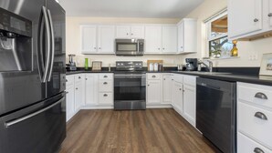 A modern kitchen with white cabinetry, stainless steel appliances, and a wooden floor. - Hawk's View- Mountain Cottage! (Jasper)