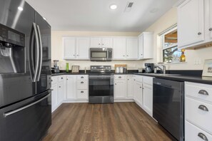 Una cucina moderna con mobili bianchi, elettrodomestici in acciaio inossidabile e pavimento in legno.