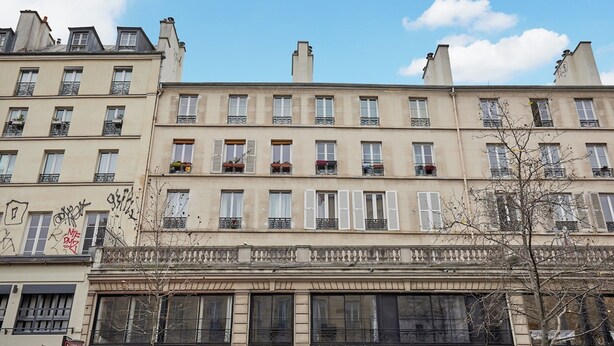 Una hilera de edificios de varios pisos con un estilo arquitectónico uniforme, con balcones y ventanas con persianas.