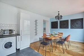 Eine moderne Küche mit weißen Schränken, einer eingebauten Waschmaschine, einer Mikrowelle und einem Essbereich mit Holztisch und Stühlen.