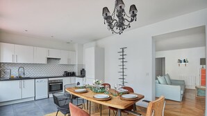 Una cocina moderna con armarios blancos, una mesa de comedor de madera para cuatro personas y una araña.