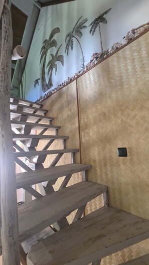 Una escalera de madera con diseño de pared tejido y obra de arte con palmeras.