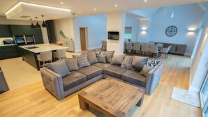 Een moderne woonkamer met een hoekbank, een houten salontafel en een eethoek met tafel en stoelen.