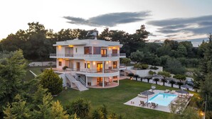 Una casa a più piani con piscina e area salotto all'aperto, immersa nel verde.