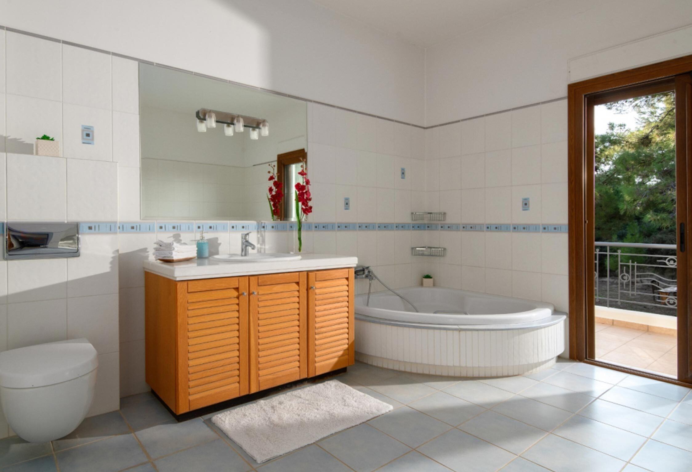 Ein modernes Badezimmer mit einem Holzbadschränkchen, einem großen Spiegel, einer Badewanne und einem WC.