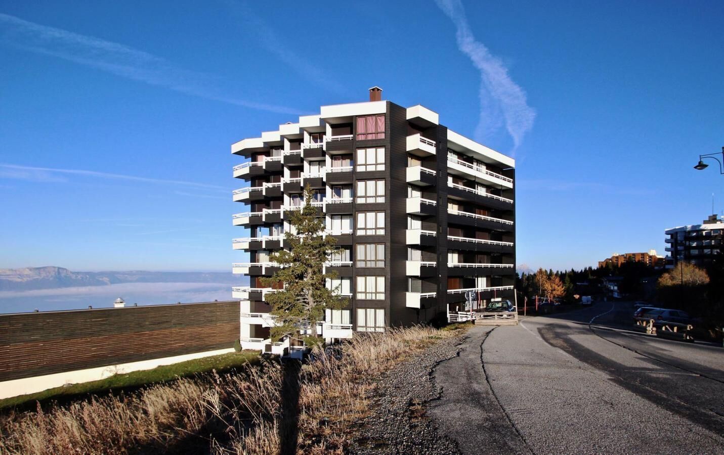 Un edificio de varios pisos con balcones, cielo despejado y vista al paisaje.