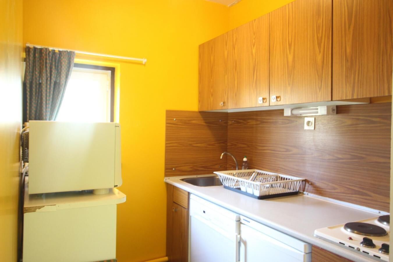 Una cocina compacta con armarios de madera, encimera blanca, pileta y estufa.