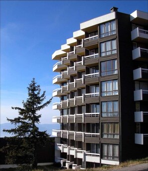 A multi-story building with balconies, large windows, and a clear sky.