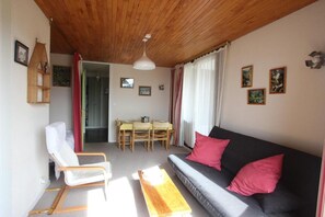 A cozy living room with a wooden ceiling, a sofa with pink cushions, a dining table with chairs, and a wooden rocking chair. - 300m from ski slopes, 5th floor, balcony, tv, 44m², Chamrousse (Chamrousse)