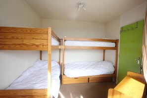 A room with three bunk beds, a green door, and a small wooden table.