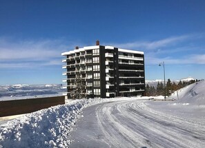 Un edificio de varios pisos con balcones, ubicado en una ladera nevada bajo un cielo despejado.
