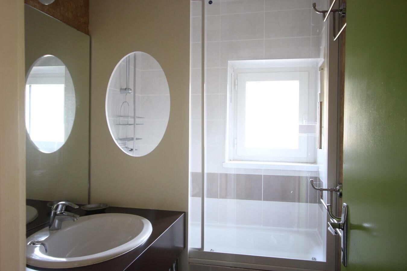 Une salle de bain avec un lavabo blanc, un miroir, un espace douche et une fenêtre.