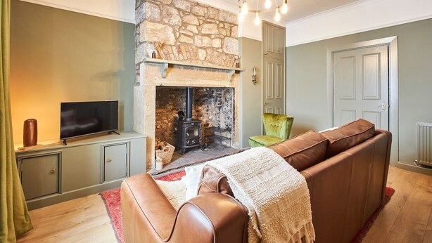 A living room with a stone fireplace, a television on a cabinet, a sofa, and a green chair.