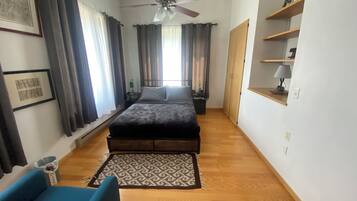 A bedroom with a bed, a blue chair, a ceiling fan, a wooden floor, and a patterned rug.