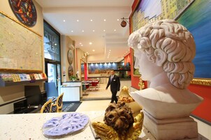 Un vestíbulo de hotel con un busto de mármol, un mapa en la pared y un área de comedor al fondo.