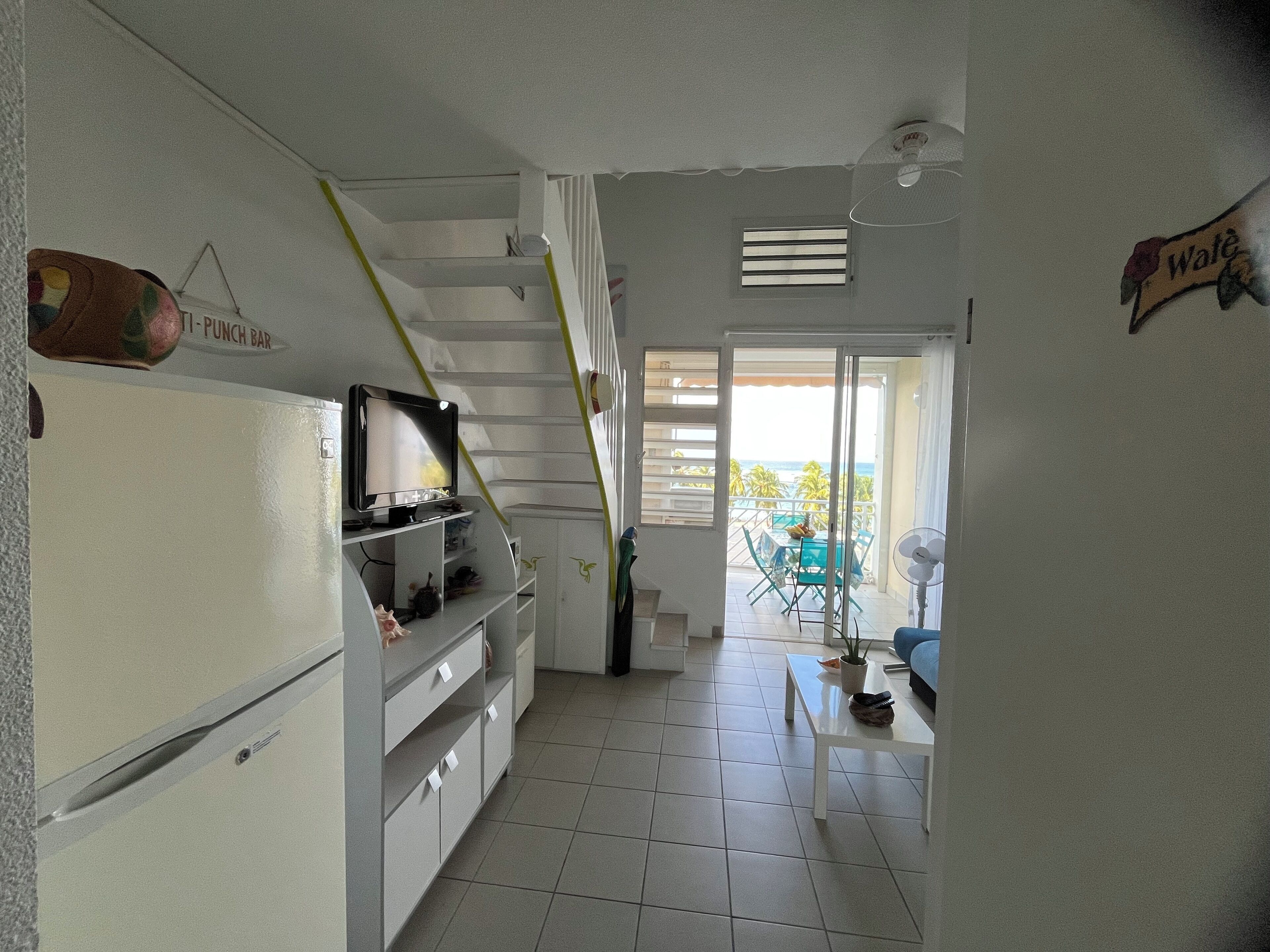 A compact living space with a kitchen, dining area, and a staircase leading to a balcony with a view.