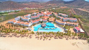 A resort with multiple buildings, a central swimming pool, and palm trees.