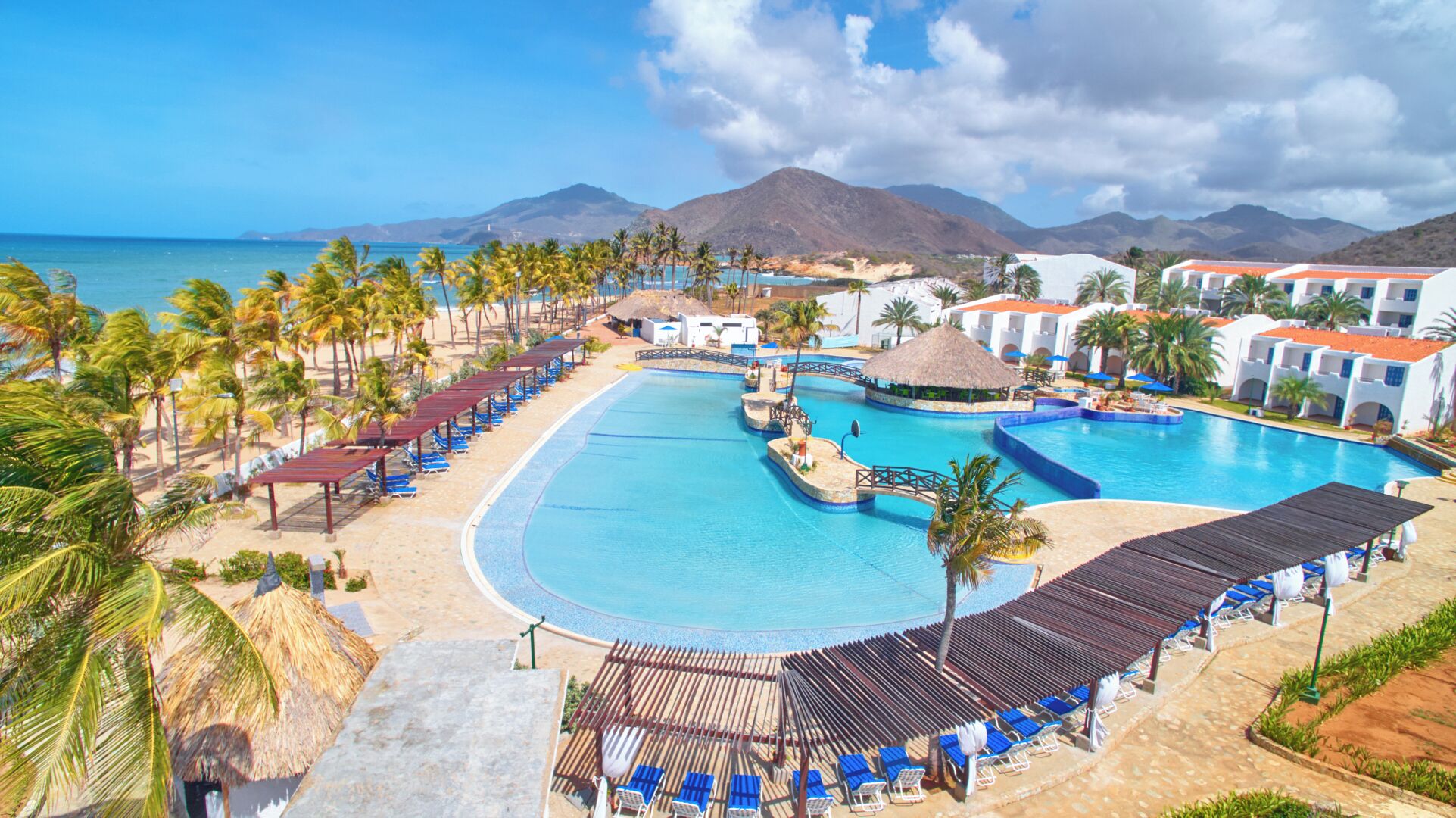 A resort with a large swimming pool, beach area, and mountain views.