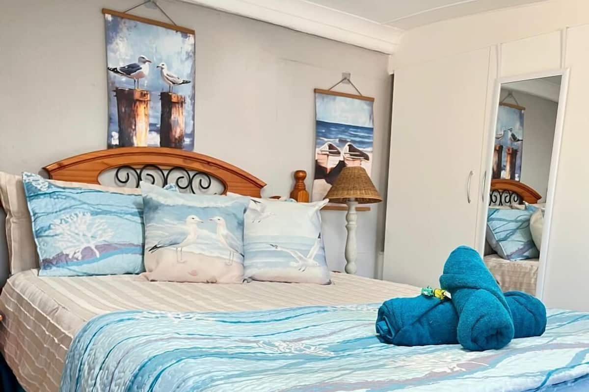 A neatly made bed with a blue and white ocean-themed duvet, pillows with seagulls, and a blue towel on the bed.