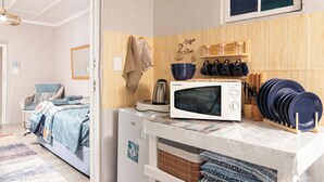 A compact kitchen with a microwave, a kettle, and a coffee maker. There are wooden cabinets and a small window above the sink. - The Fisherman's Porch (Bergrivier)