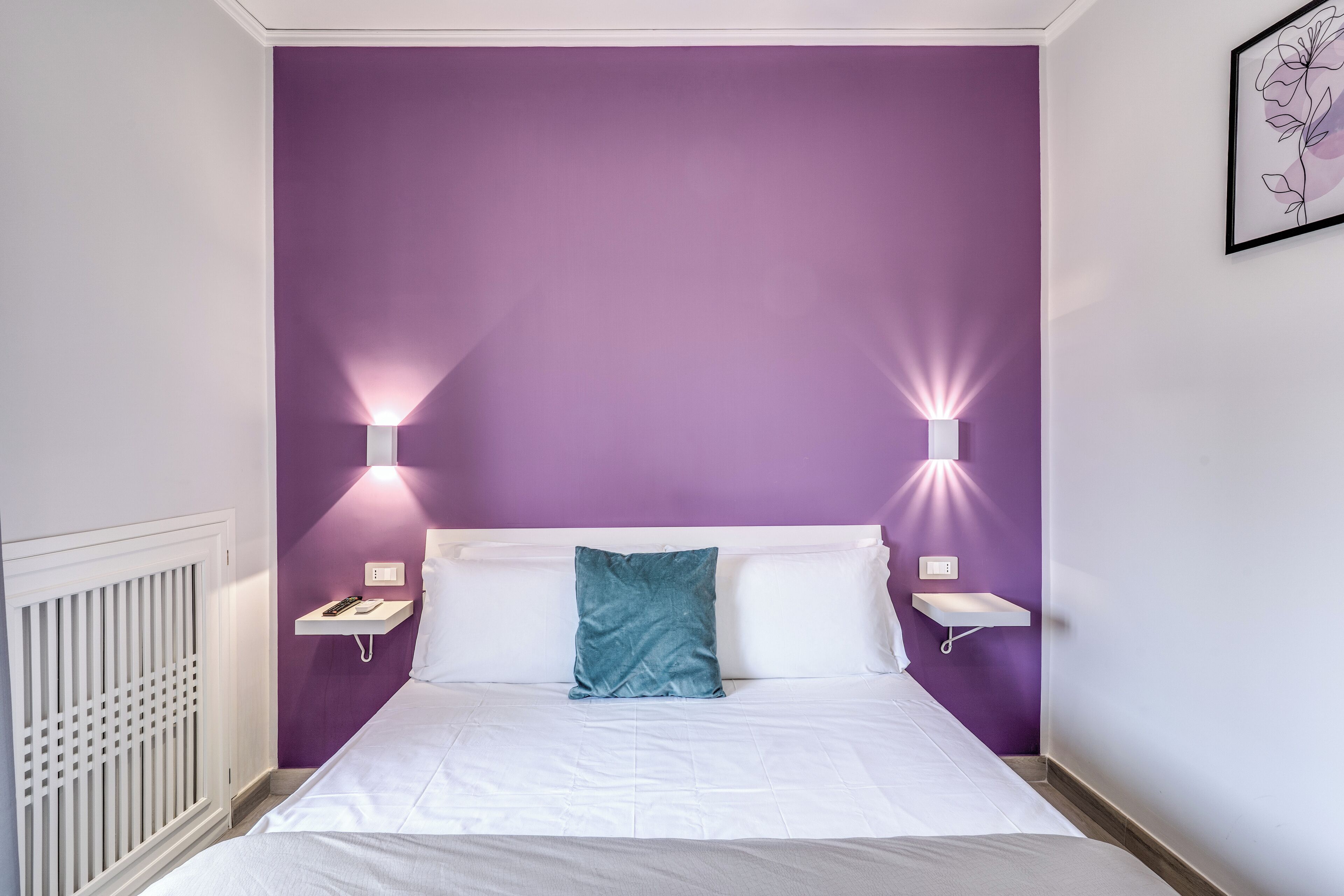 Ein ordentlich bezogenes Bett mit weißen Leinen, einem türkisblauen Kissen und zwei Nachttischen mit Lampen.