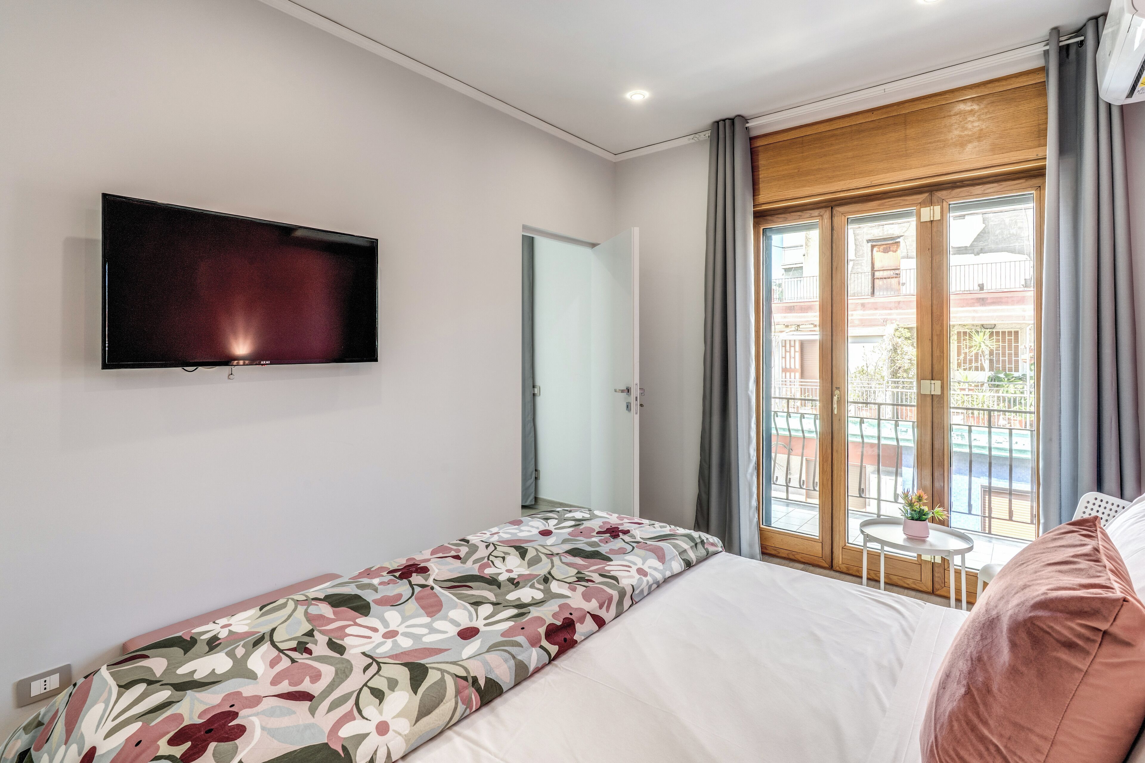 Ein Schlafzimmer mit einem Bett, einem an der Wand befestigten Fernseher, einem Fenster mit Ausblick und einem kleinen Tisch mit einer Pflanze.