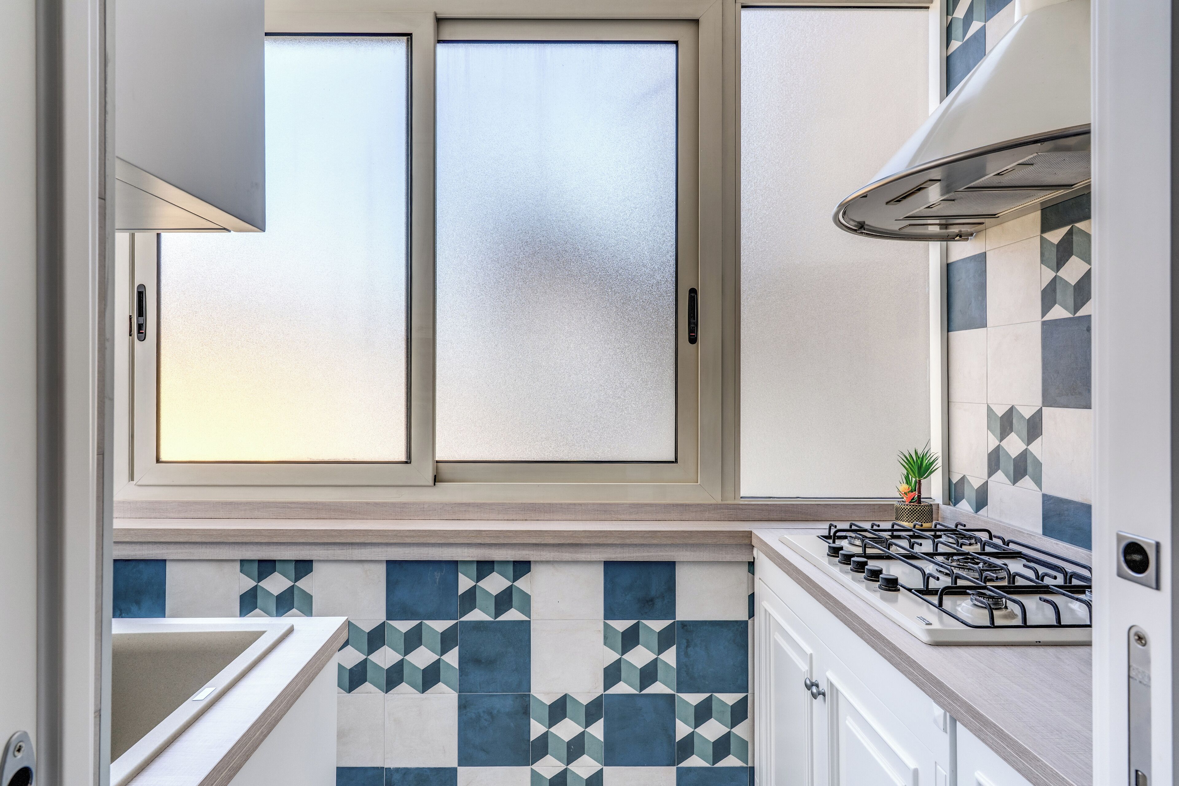 A kitchen with a gas stove, a window with frosted glass, and a tiled backsplash.