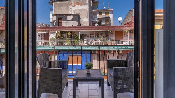 A balcony with wicker chairs and a small table, overlooking a building with balconies and a pool. - Marmolo Room (Naples)