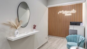 A modern reception area with a wooden panel wall, a neon sign reading "Marmolo Room," a white reception desk, a blue chair, and a white shelf with a vase and decorative items. - Marmolo Room (Naples)