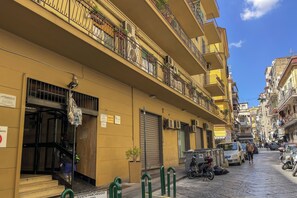 A narrow street with yellow buildings, balconies, and parked scooters. - Marmolo Room (Naples)