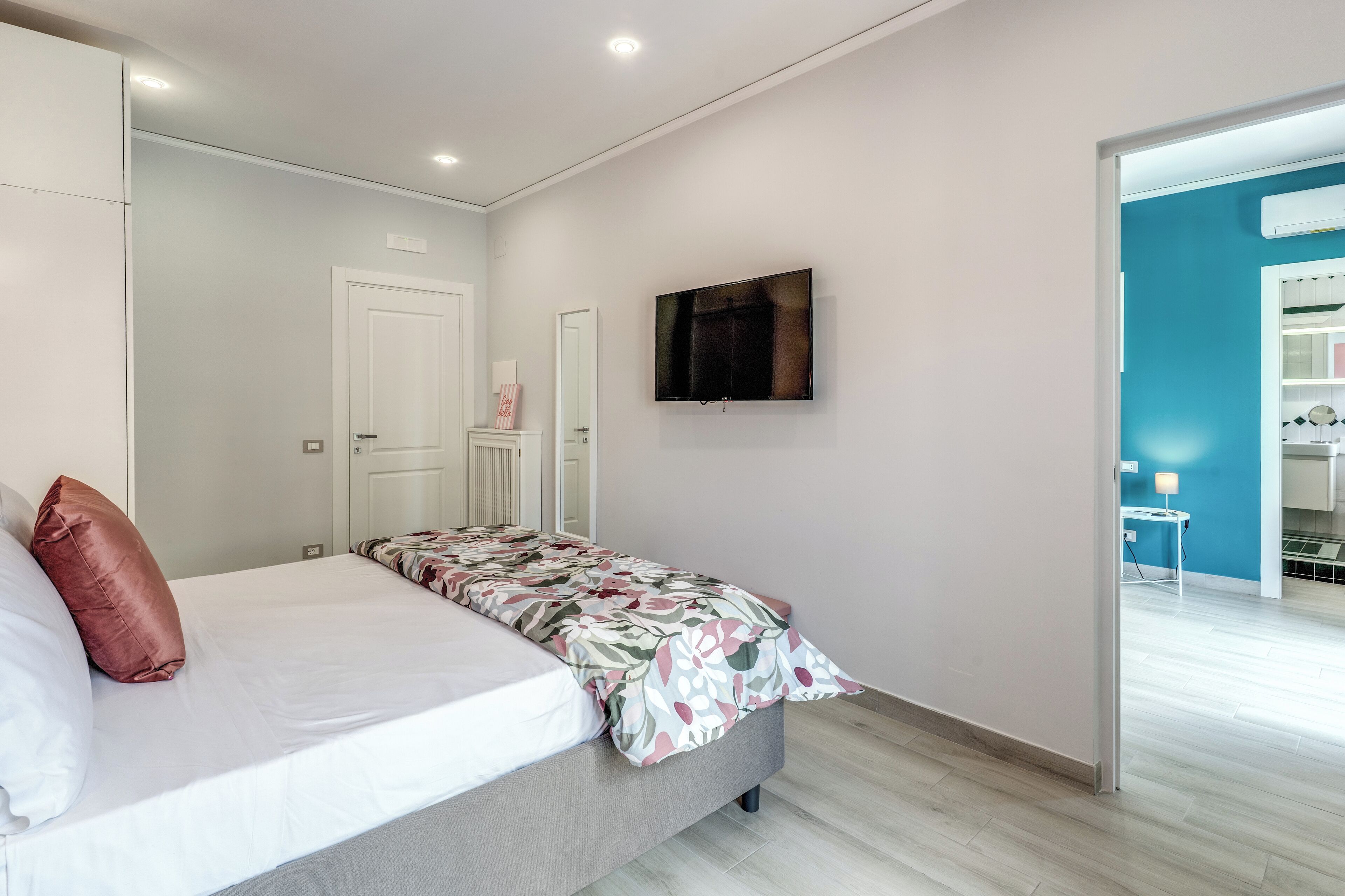 A bedroom with a bed, a TV mounted on the wall, and a door leading to another room.