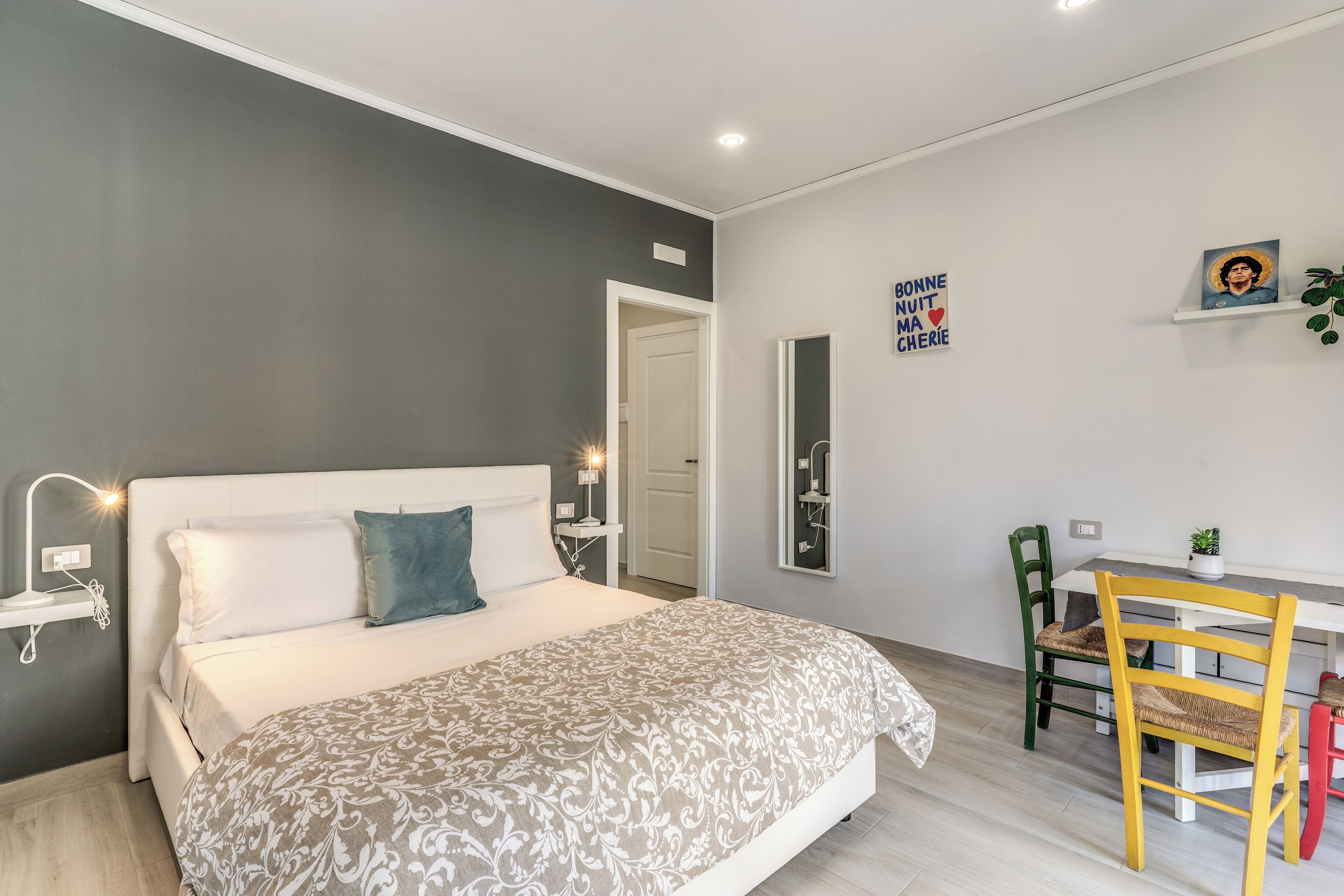 A bedroom with a bed, bedside table, lamp, and a desk with chairs.