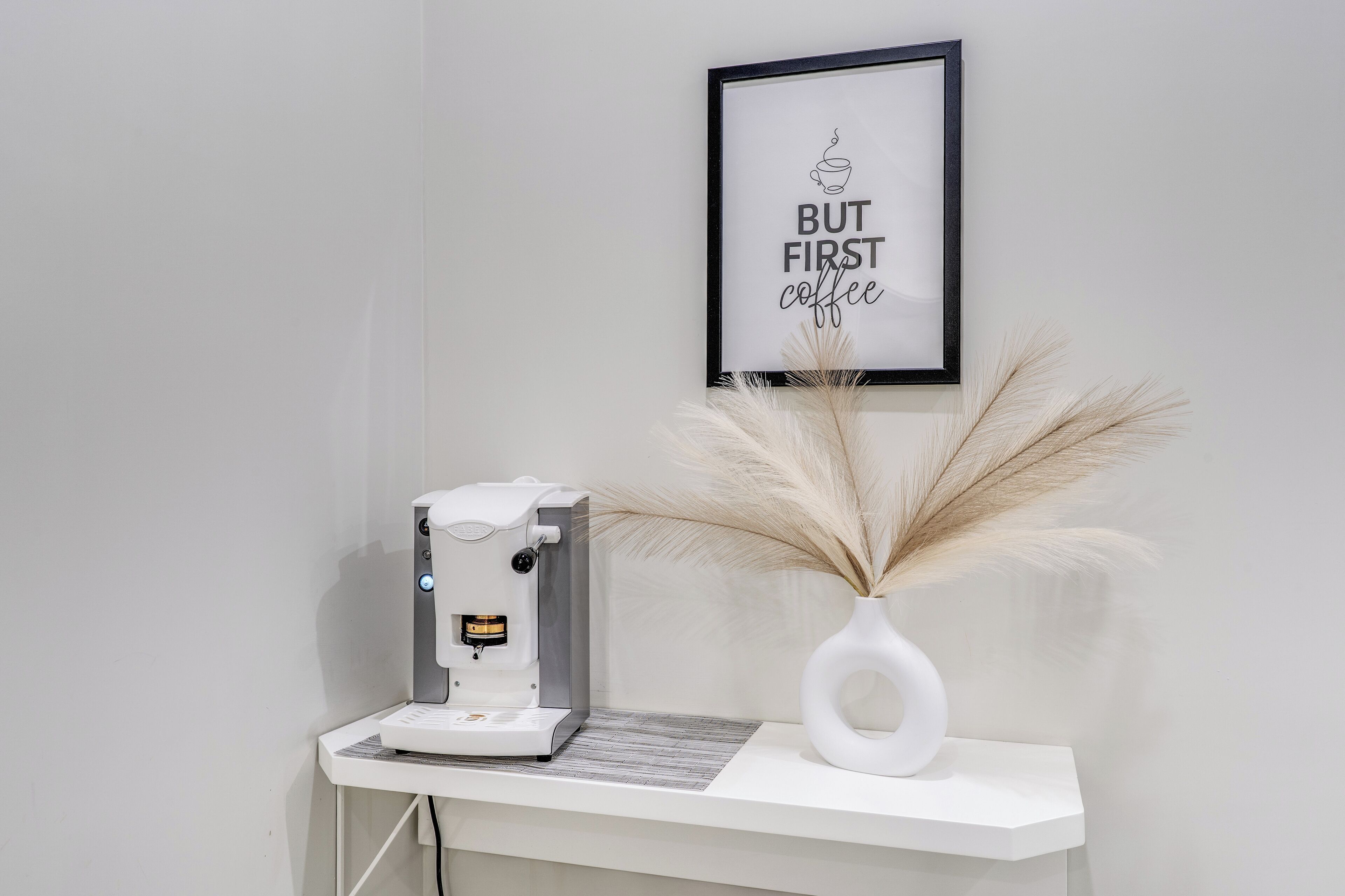 En kaffemaskine på en hvid bordplade med et indrammet skilt over.