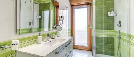 A modern bathroom with a glass-enclosed shower, a large mirror, and a vanity with a sink and storage.