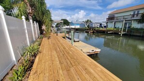 A wooden dock extending into calm water, surrounded by a white fence and greenery. - All Decked Out (St. Augustine)