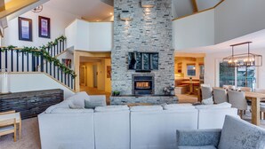A spacious living area with a stone fireplace, a large sofa, and a dining area with a wooden table and chairs. - Pet friendly chalet right on the ski way, steps from tube town pet friendly too! (Silver Star Mountain)