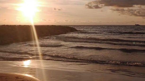 A beach scene with the sun setting over the ocean, waves gently lapping at the shore, and a distant ship on the horizon. - Castle house (Cartagena)