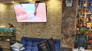 A living room with a blue sofa, a flat-screen TV mounted on a textured wall, a dining table with chairs, and a decorative plant on the table. - Castle house (Cartagena)
