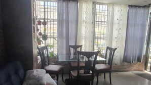 A living room with a blue sofa, a glass-top dining table with chairs, and a view through large windows with curtains. - Castle house (Cartagena)