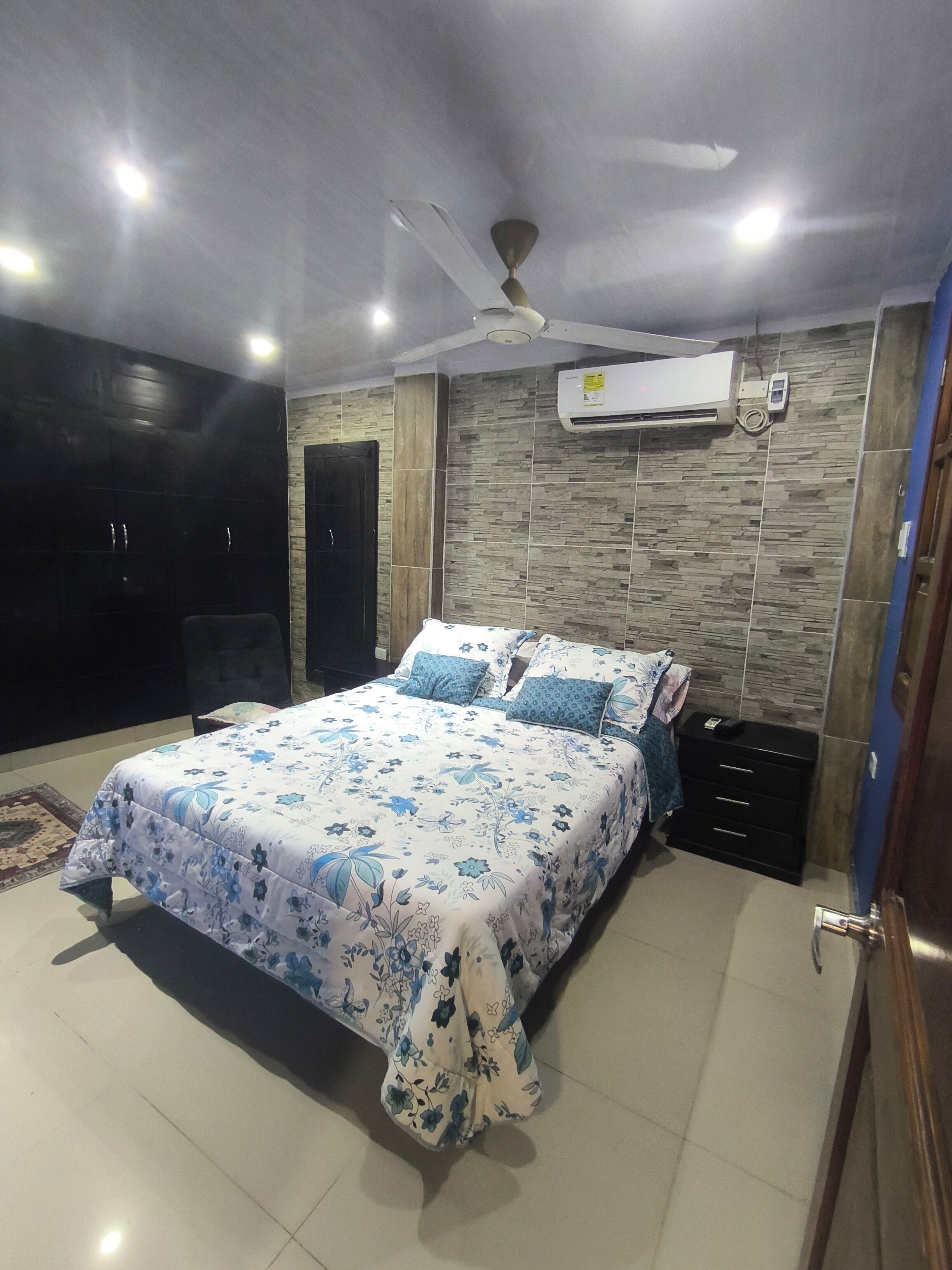 Une chambre à coucher comprenant un lit, un ventilateur de plafond, un appareil de climatisation, une armoire et une table de chevet.